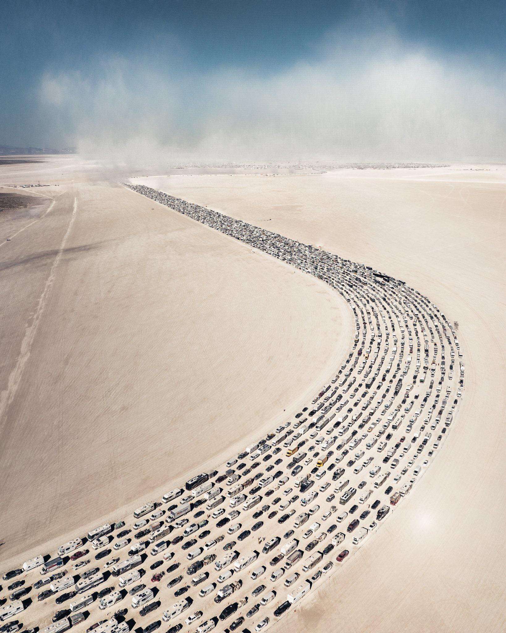 Aerial view of a long, winding parking lot filled with cars in the desert.