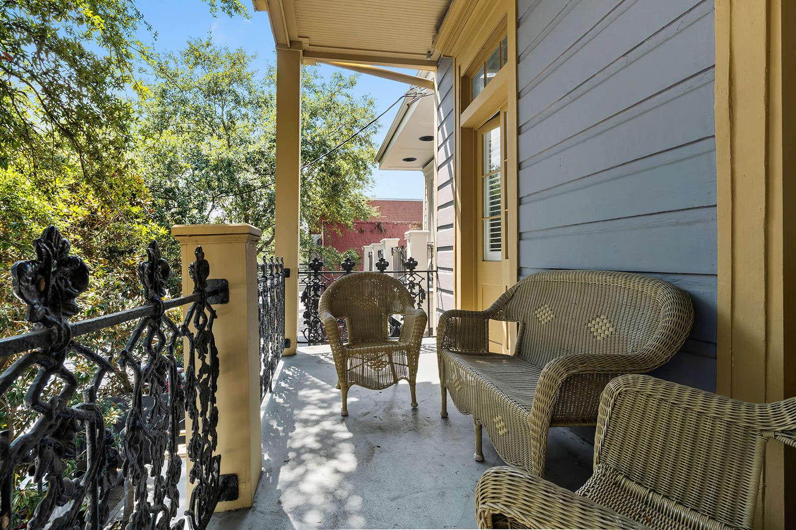 A balcony with wicker furniture and a black railing overlooking trees and a blue sky.