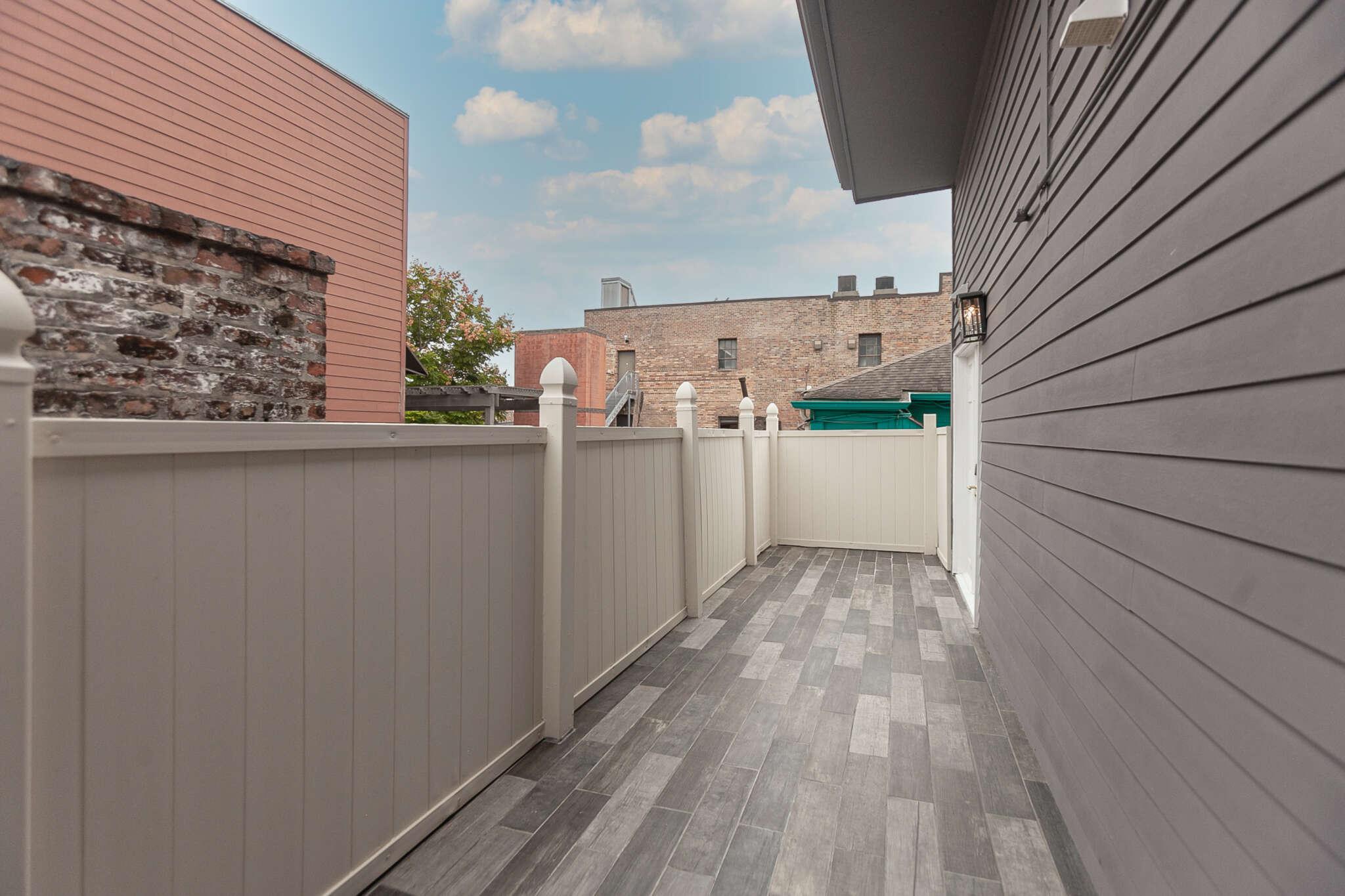 A fenced patio area with a gray tile floor, overlooking the city under a blue sky.
